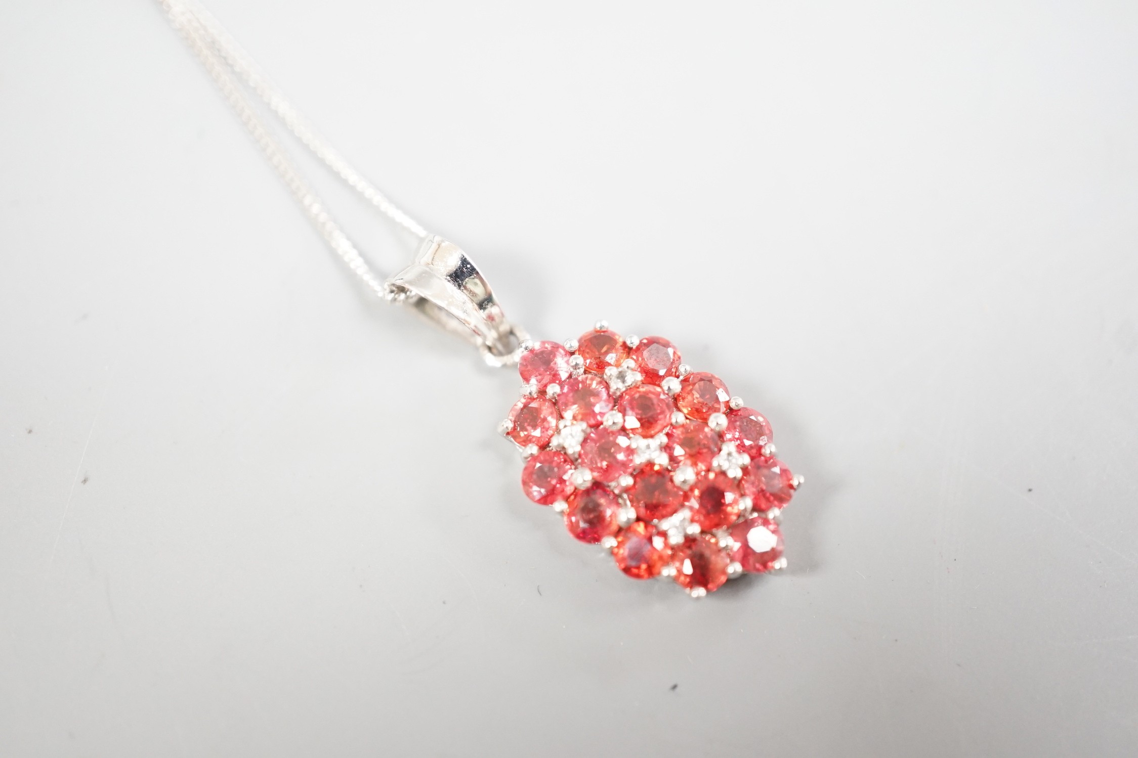 A modern 375 white metal, sunset ruby and white sapphire set cluster pendant, 19mm, on a 375 white metal chain, 42cm, gross 4 grams, with Rocks & Co certificate.